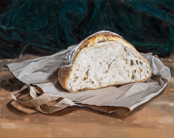 A cut loaf of sourdough bread resting on a paper bag with a green fabric background