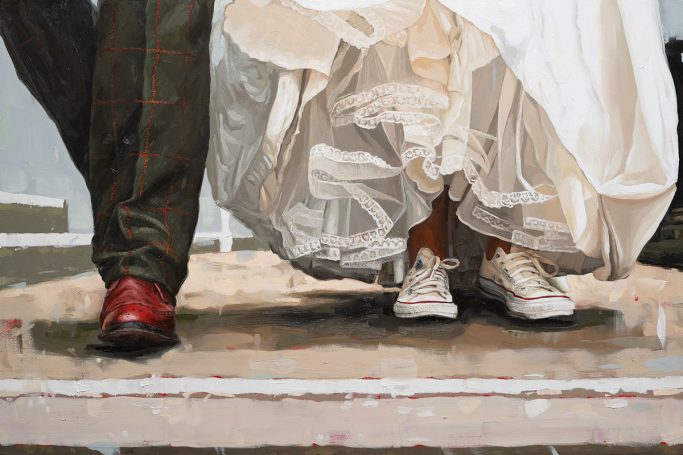 Close-up of a bride in a white dress wearing Converse shoes beside a groom in dress shoes.