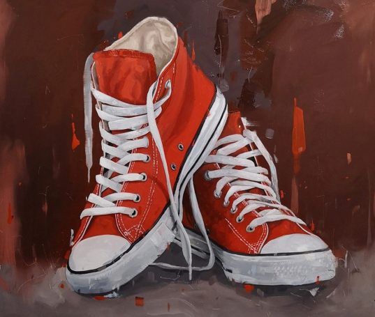 Pair of orange high-top canvas trainers with white laces against a textured dark background.